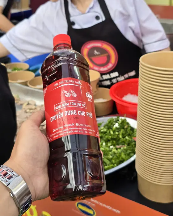 Bàn tay cầm chai nước mắm Tôm Cọp Đỏ chuyên dùng cho phở cạnh khay hành lá và chồng bát